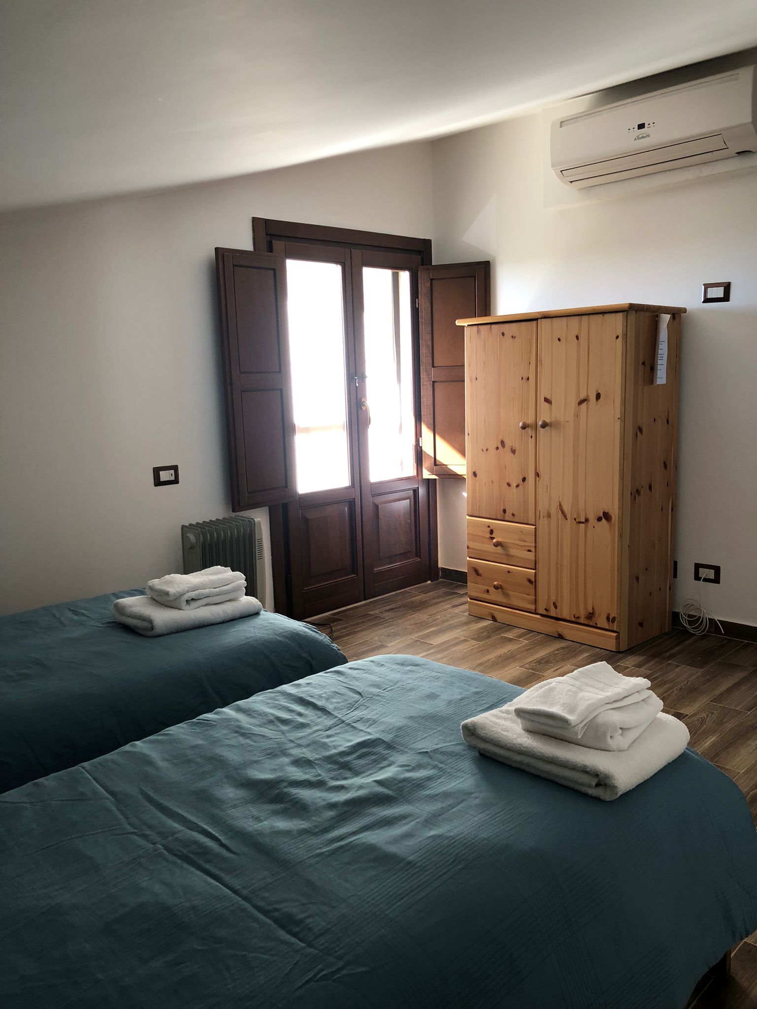 foto di una camera da letto su una mansarda con due lettini, pavimento in legno e armadio
