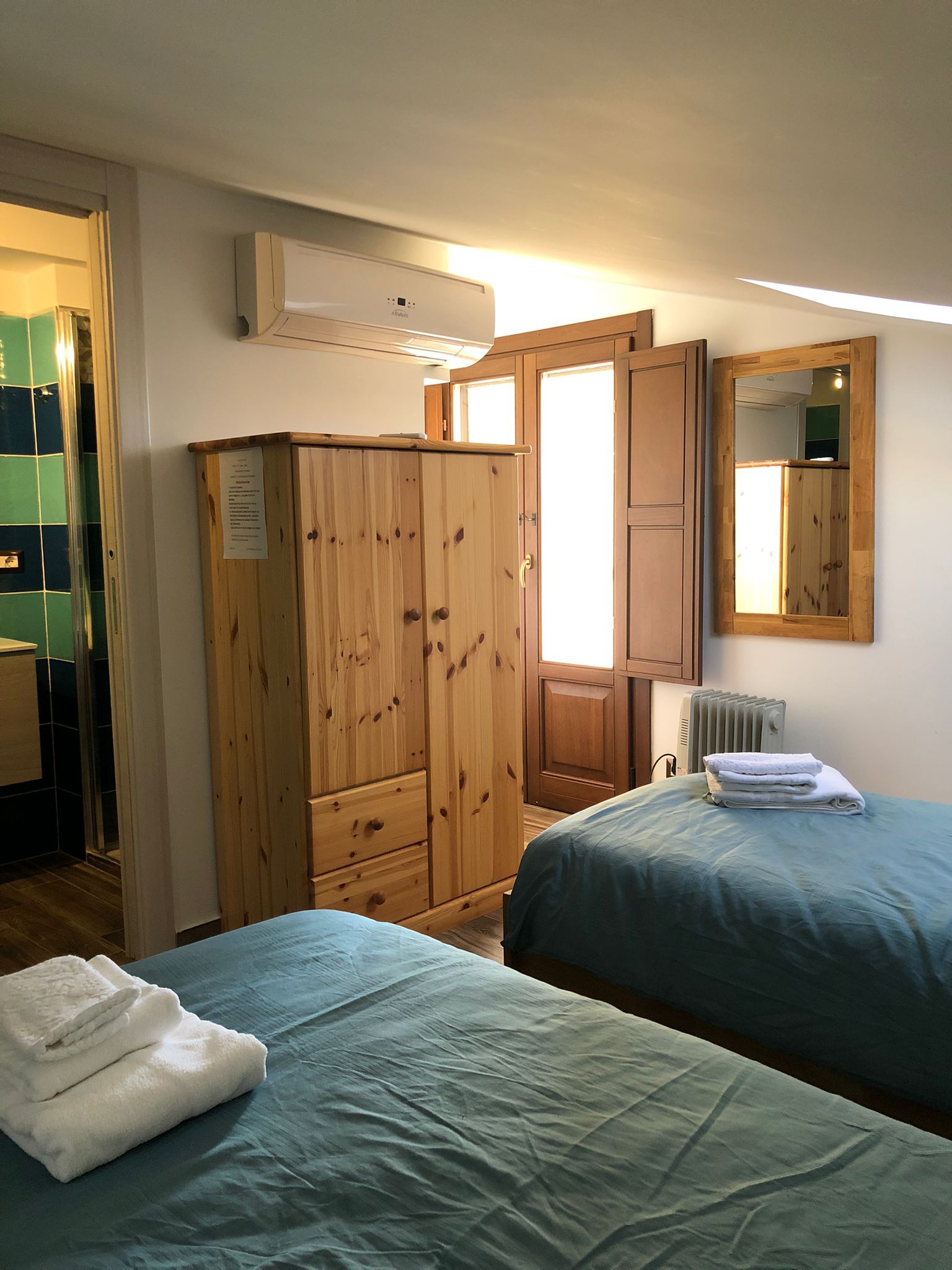 foto di una camera da letto su una mansarda con due lettini, pavimento in legno e bagno in camera